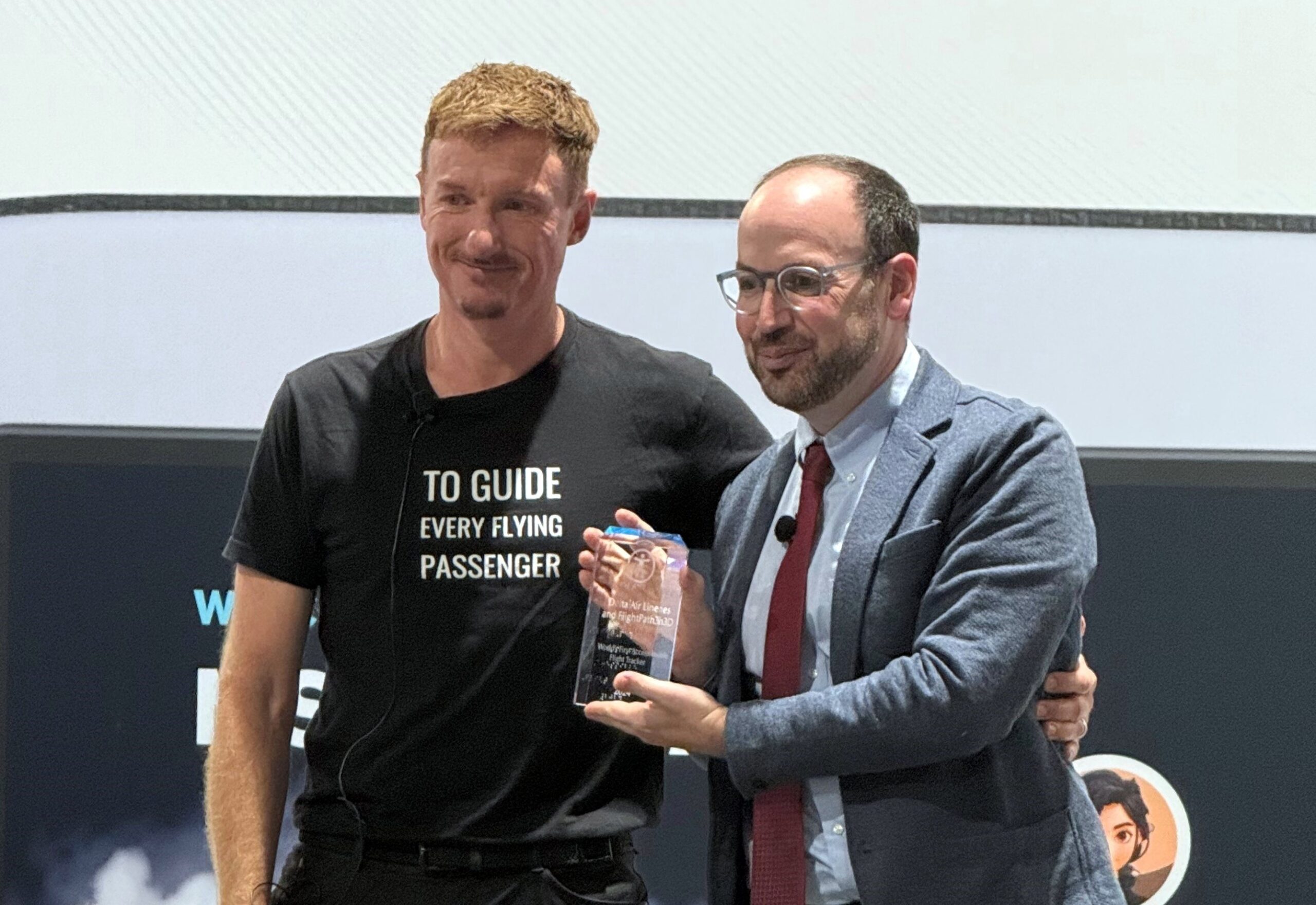 FlightPath3D President Duncan Jackson presents Delta's Ekrem Dimbiloglu with an award (including braile) celebrating activation of the first accessibility map on a plane. FlightPath3D President Duncan Jackson presents Delta's Ekrem Dimbiloglu with an award (including braille) celebrating activation of the first accessibility map on a plane.