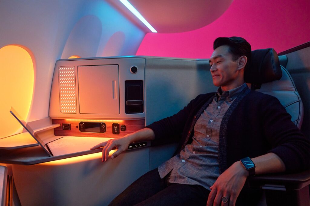 Man sitting in a premium seat with soft yellow and magenta lighting.