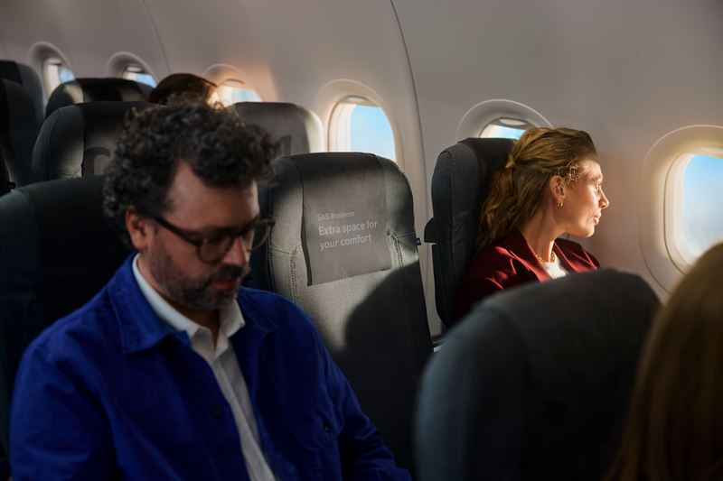 A man and a woman sitting in SAS Business Class seats with an empty middle seat between them.