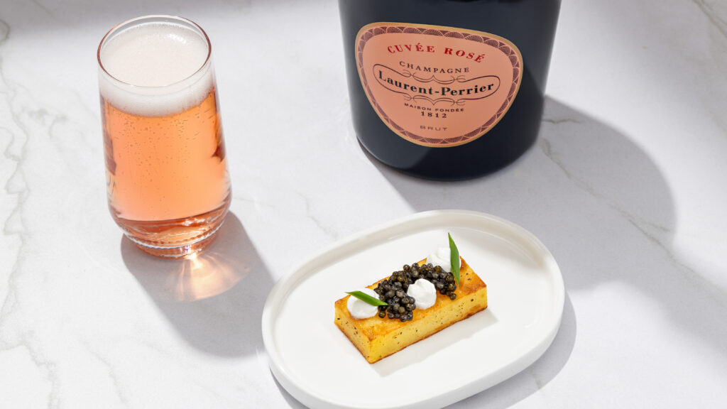 Laurent-Perrier Cuvee Rose champagne bottle and a glass of pink bubbly next to a small bite of maybe polenta with a bit of caviar on top.