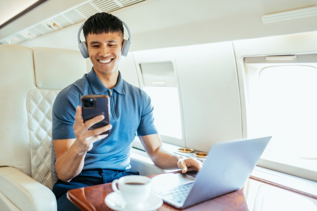 Guy sitting on a private jet using both a personal device and a laptop