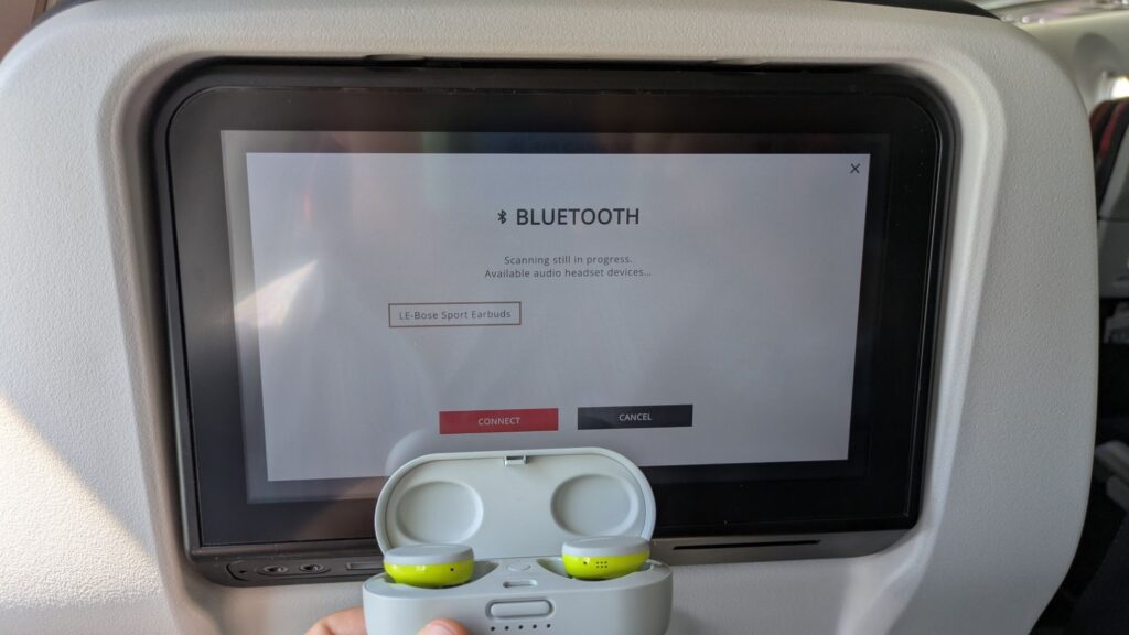 Bluetooth earbuds in front of an IFE screen showing the pairing process.