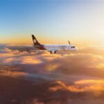 rendering of an Aeromexico E190 flying above the clouds with orange sunlight lighting things up