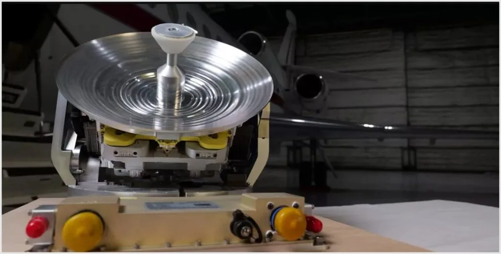 Shiny silver Honeywell JetWave X antenna on a table in front of a business jet.