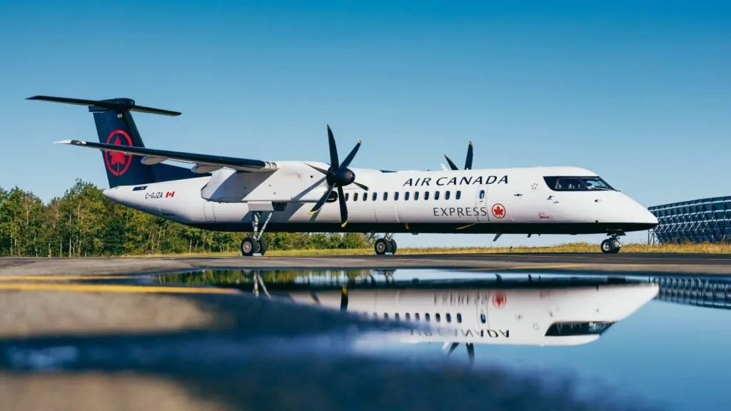 Air Canada Jazz Q400 parked in front of a puddle to create a reflection. It has the Starlink antenna installrd.