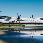 Air Canada Jazz Q400 parked in front of a puddle to create a reflection. It has the Starlink antenna installrd.