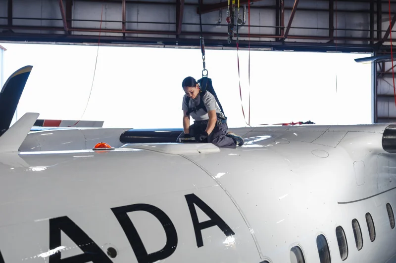 mechanic kneeling atop an airplane