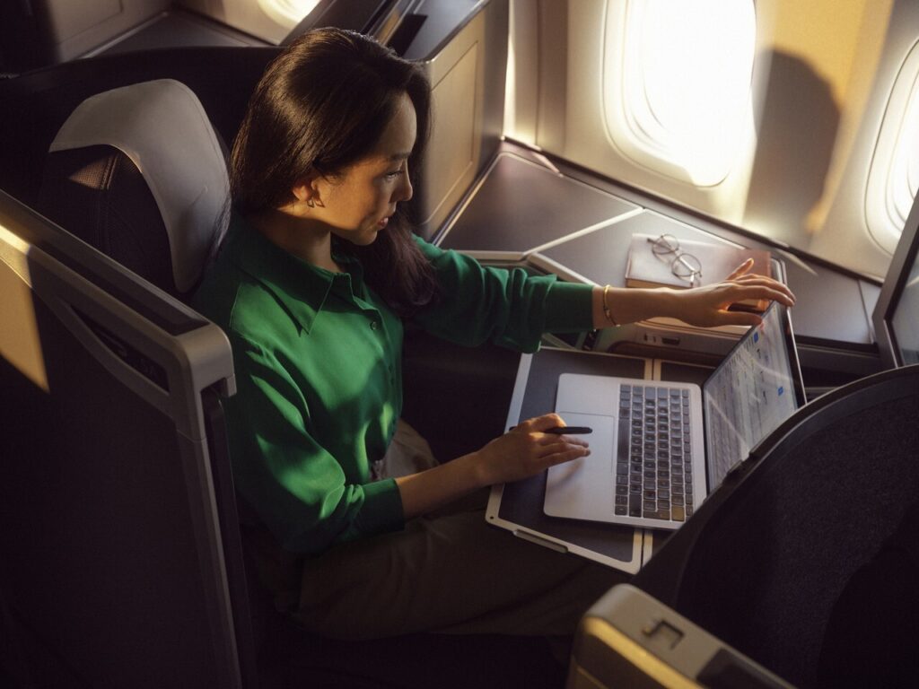 A woman using a laptop in a business class seat on a plane.