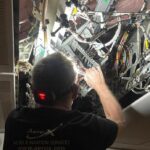back of a guy's head working in the space behind the overhead panels on a plane, installing a WiFi router and access point.