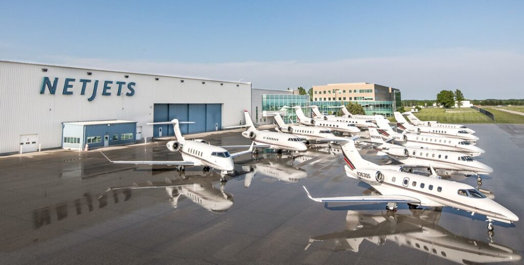 Many private jets of different types parked in front of a NetJets hangar