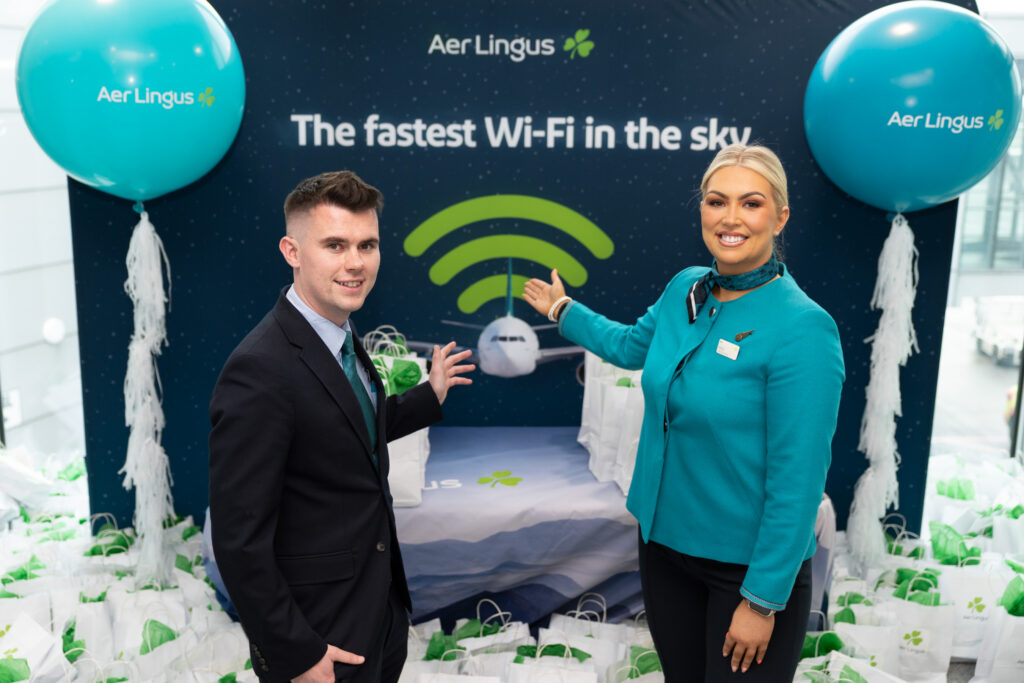 Two airline crew members pointing to a sign advertising the new Aer Lingus inflight wi-fi powered by Starlink at a pre-flight ceremony