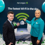 Two airline crew members pointing to a sign advertising the new Aer Lingus inflight wi-fi powered by Starlink at a pre-flight ceremony
