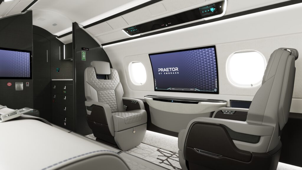 Interior of a business jet, including lounge seating and a 42-inch curved IFE screen embedded in the wall.