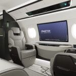 Interior of a business jet, including lounge seating and a 42-inch curved IFE screen embedded in the wall.