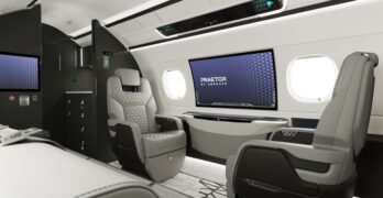 Interior of a business jet, including lounge seating and a 42-inch curved IFE screen embedded in the wall.