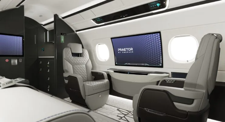 Interior of a business jet, including lounge seating and a 42-inch curved IFE screen embedded in the wall.
