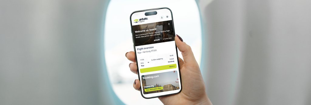 hand holding an iPhone in front of a plane window. The screen shows the new airBaltic shopping portal, including flight details and an option to book a hotel via a partner.