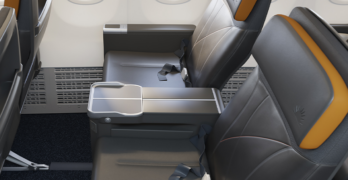 Rendering of the new Allegiant First seats, mostly grey with orange highlights and the company's sunburst logo embossed on the headrest.