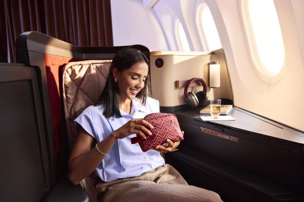 woman gazing longingly into a business class amenity kit while in a business class seat on an airplane
